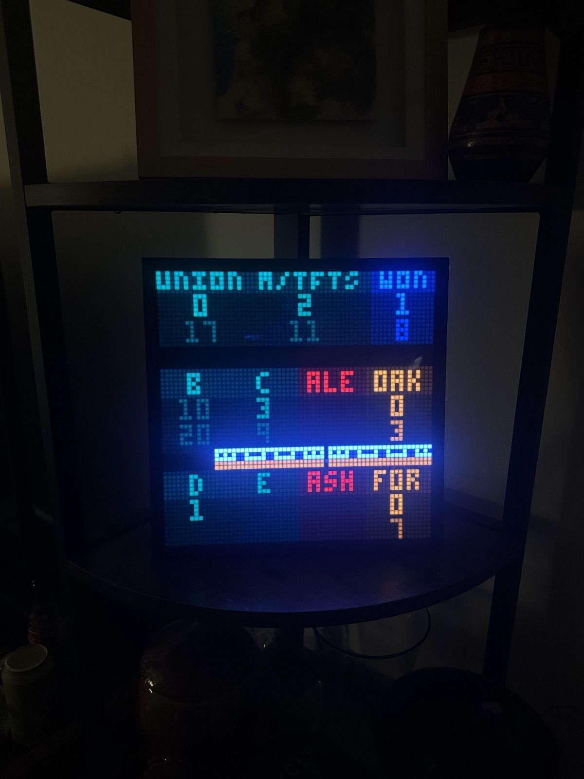 The Pixoo display on a shelf showing train times, with an orange line train crossing the middle of the screen